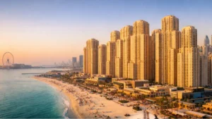 Golden-hour aerial view of Jumeirah Beach Residence beachfront towers in Dubai, showing luxury high-rise apartments, sandy beach, Arabian Gulf coastline, and vibrant promenade lifestyle.