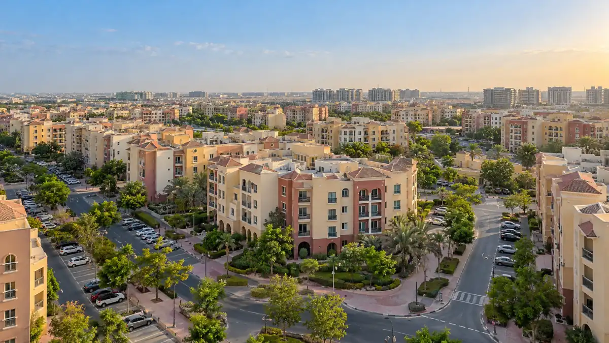 Aerial view of International City in Dubai, featuring colourful residential apartment buildings, landscaped green spaces, tree-lined streets and modern urban infrastructure.